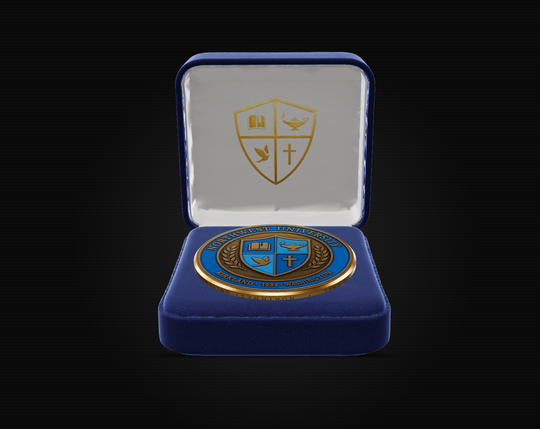 An open royal blue velvet presentation box with a gold crest on the inner lid, displaying a round blue and gold enamel medal or coin on a black background.