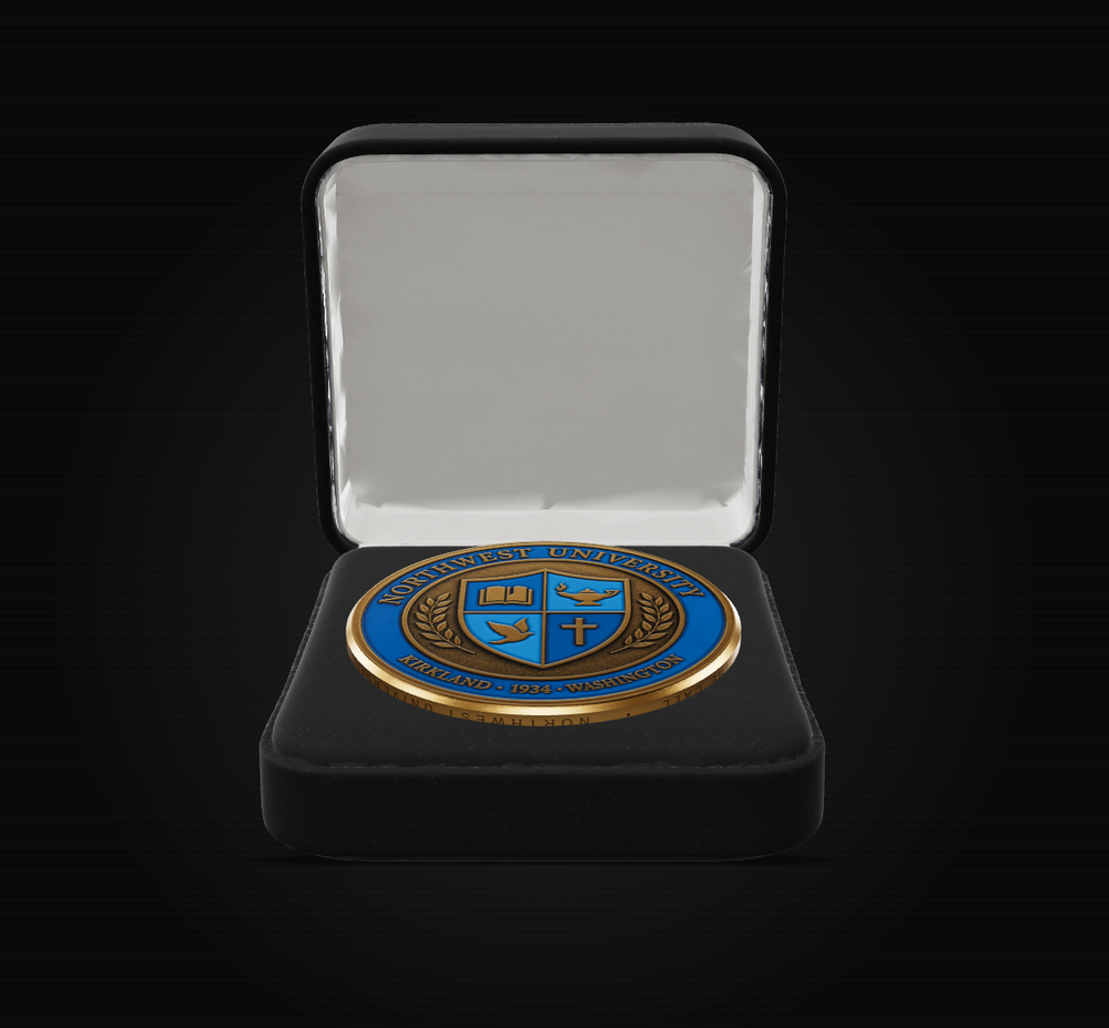 A round blue and gold challenge coin featuring the University of Notre Dame crest, presented inside an open black velvet jewelry box with a white satin lining, set against a solid black background.
