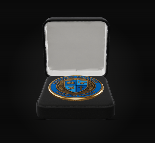 A round blue and gold challenge coin featuring the University of Notre Dame crest, presented inside an open black velvet jewelry box with a white satin lining, set against a solid black background.