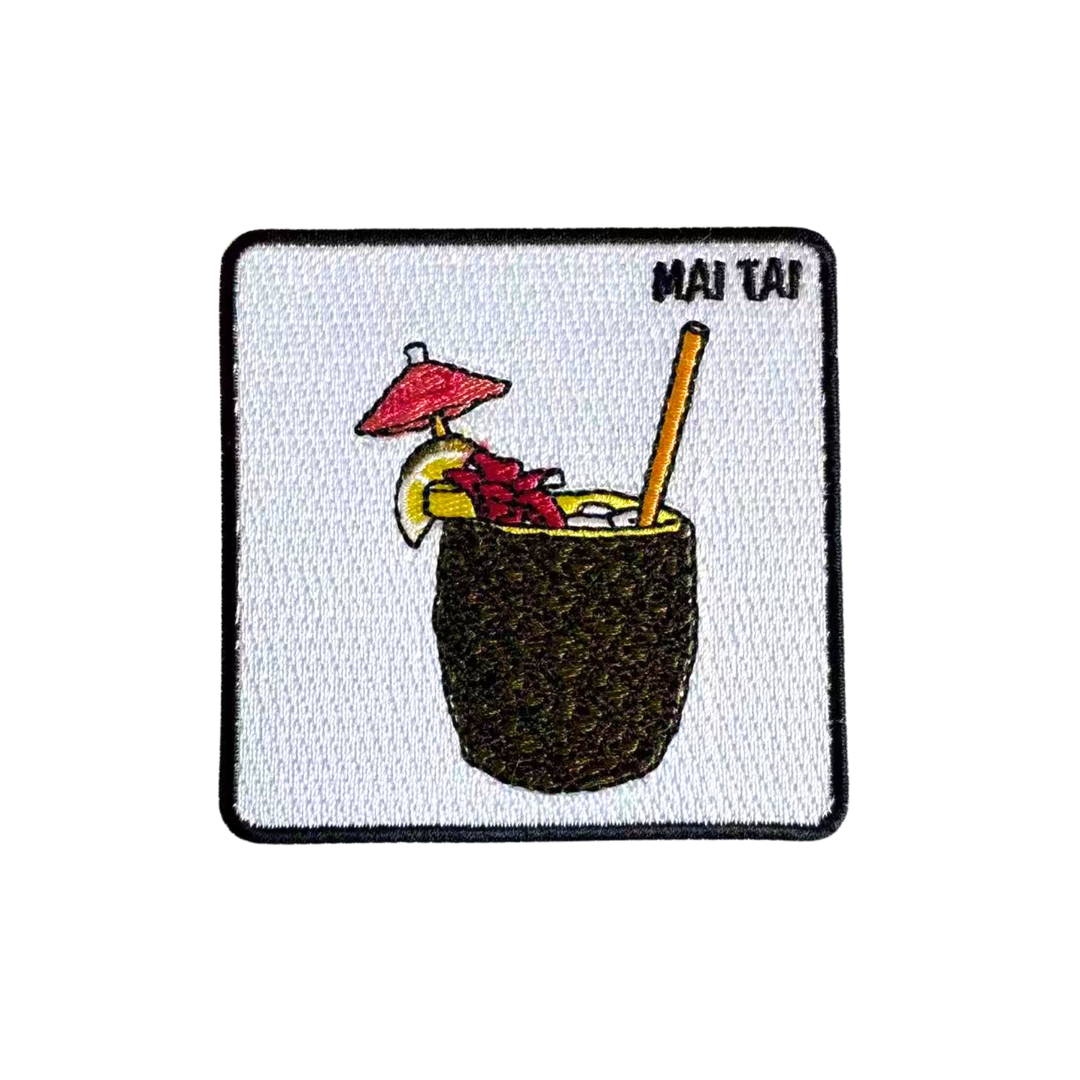 An embroidered patch featuring a 'Mai Tai' cocktail in a coconut cup with a red umbrella, yellow citrus slice, and straw, on a white background with a black border.