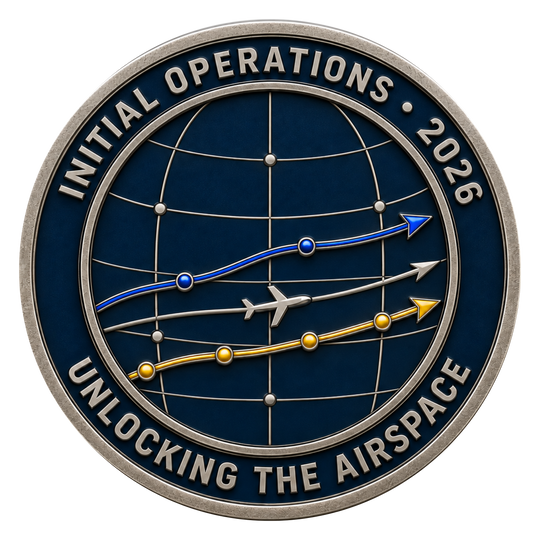 A circular commemorative coin or medallion with a dark blue globe design, silver-toned border and text reading 'INITIAL OPERATIONS • 2026' and 'UNLOCKING THE AIRSPACE,' plus blue, gray, and gold flight-path graphics and a small airplane icon.
